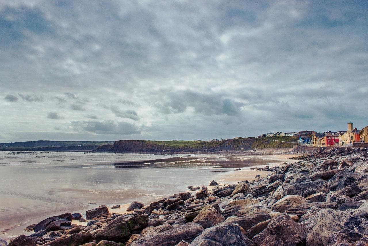 Rocky Irish coastline with colorful cliffside houses in the distance
